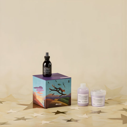 Cosmetic products including a bottle, a box with a desert design, and two containers on a beige surface.