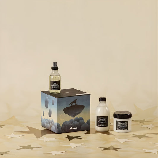 Aveda products including a bottle, box, and jar on a beige surface with a minimal background.